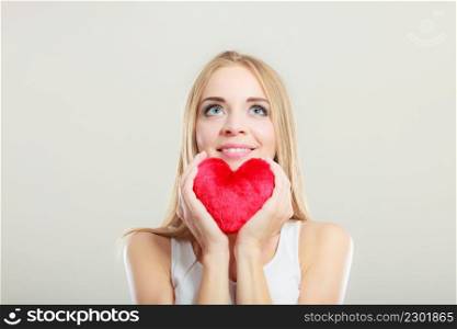 Valentines day love and relationships concept. Blonde long hair young woman holding red heart love symbol studio shot on gray