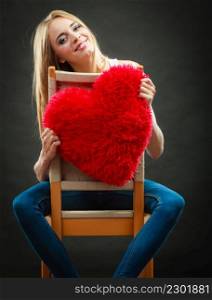 Valentines day love and relationships concept. Blonde long hair young woman holding heart shaped pillow love symbol on dark background