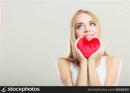 Valentines day love and relationships concept. Blonde long hair young woman holding red heart love symbol studio shot on gray
