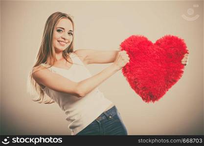 Valentines day love and relationships concept. Blonde long hair young woman holding heart shaped pillow love symbol filtered photo
