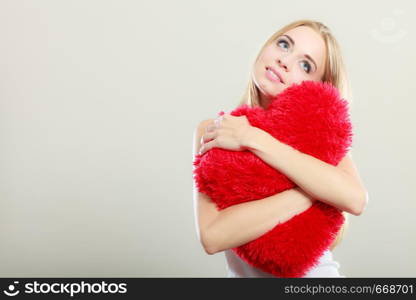 Valentines day love and relationships concept. Blonde long hair young woman hugging heart shaped pillow love symbol