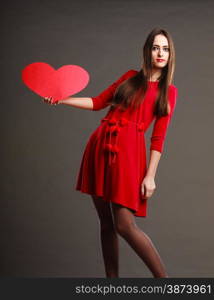 Valentines day love and relationships concept. Brunette long hair young woman in red dress holding heart love symbol dark gray background