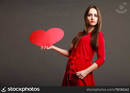 Valentines day love and relationships concept. Brunette long hair young woman in red dress holding heart love symbol dark gray background