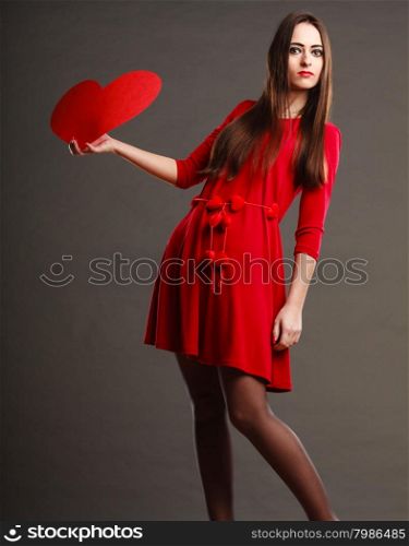 Valentines day love and relationships concept. Brunette long hair young woman in red dress holding heart love symbol dark gray background