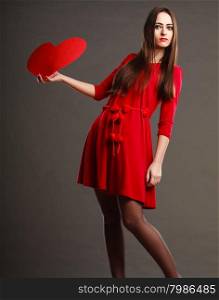 Valentines day love and relationships concept. Brunette long hair young woman in red dress holding heart love symbol dark gray background