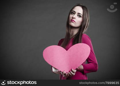 Valentines day love and relationships concept. Brunette long hair young woman in fuchsia dress holding heart love symbol dark gray background