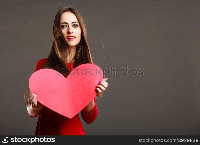 Valentines day love and relationships concept. Brunette woman long hair girl in red outfit holding heart love symbol, text area dark gray background