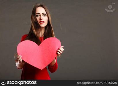 Valentines day love and relationships concept. Brunette woman long hair girl in red outfit holding heart love symbol, text area dark gray background