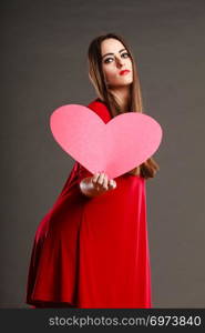 Valentines day love and relationships concept. Brunette woman long hair girl in red outfit holding heart love symbol dark gray background