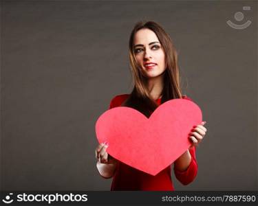 Valentines day love and relationships concept. Brunette woman long hair girl in red outfit holding heart love symbol, text area dark gray background