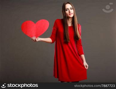 Valentines day love and relationships concept. Brunette woman long hair girl in red outfit holding heart love symbol dark gray background