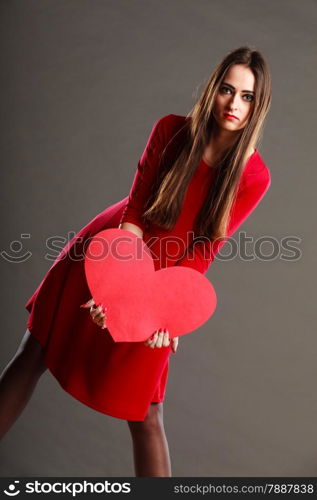 Valentines day love and relationships concept. Brunette woman long hair girl in red outfit holding heart love symbol dark gray background