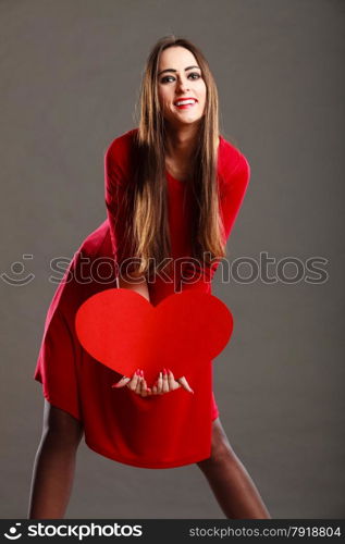 Valentines day love and relationships concept. Brunette woman long hair girl in red outfit holding heart love symbol dark gray background