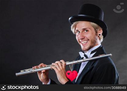 Valentines day love melody concept. Flute music playing male flutist musician performer. Young elegant stylish guy with instrument and red heart. Male flutist with flute and heart. Love melody