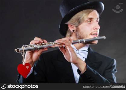 Valentines day love melody concept. Flute music playing male flutist musician performer. Young elegant stylish guy with instrument and red heart. Male flutist with flute and heart. Love melody