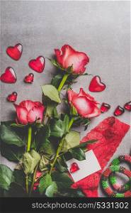 Valentines day, love or dating concept. Red roses bunch with gift box, blank paper greeting card and hearts on gray background , top view, mock up