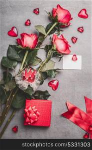 Valentines day, love or dating concept. Red roses bunch with gift box, blank paper greeting card, ribbon and hearts , top view, mock up