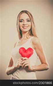 Valentines day love relationships or health care concept. Blonde young woman holding red heart love symbol on her chest studio shot
