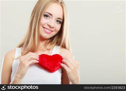 Valentines day love relationships or health care concept. Blonde young woman holding red heart love symbol on her chest studio shot on gray
