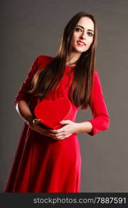 Valentines day, love, romance concept. Brunette woman long hair girl in red dress holding heart shaped gift box dark gray background