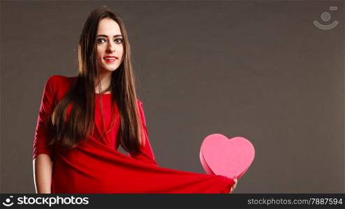 Valentines day, love, romance concept. Brunette woman long hair girl in red dress holding heart shaped gift box dark gray background