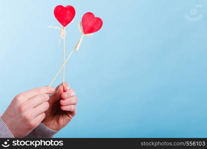 Valentines Day. Male hand holding showing red little hearts on sticks. Man presents palm with love sign symbols.. Male hand with little hearts on sticks.