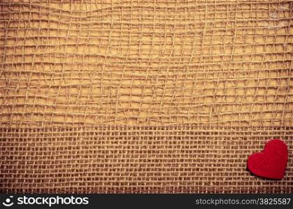 Valentines day or wedding concept. Red wooden decorative heart bagging ribbon on abstract cloth burlap background with copy space. Vintage aged tone