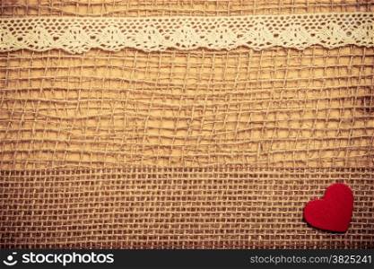 Valentines day or wedding concept. Red wooden decorative heart lace ribbon on abstract cloth burlap background with copy space. Vintage aged tone