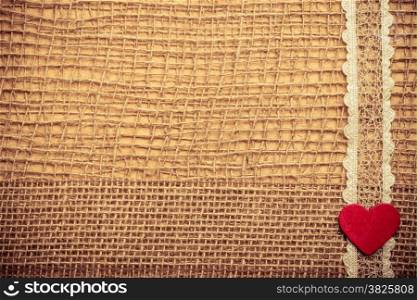 Valentines day or wedding concept. Red wooden decorative heart lace ribbon on abstract cloth burlap background with copy space. Vintage aged tone