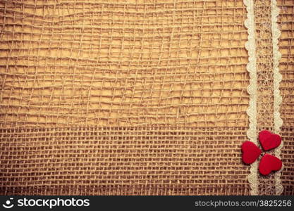 Valentines day or wedding concept. Red wooden decorative hearts lace ribbon on abstract cloth burlap background with copy space. Vintage aged tone