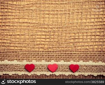 Valentines day or wedding concept. Red wooden decorative hearts lace ribbon on abstract cloth burlap background with copy space. Vintage aged tone