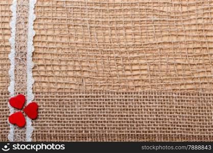 Valentines day or wedding concept. Red wooden decorative hearts lace ribbon on abstract cloth burlap background with copy space