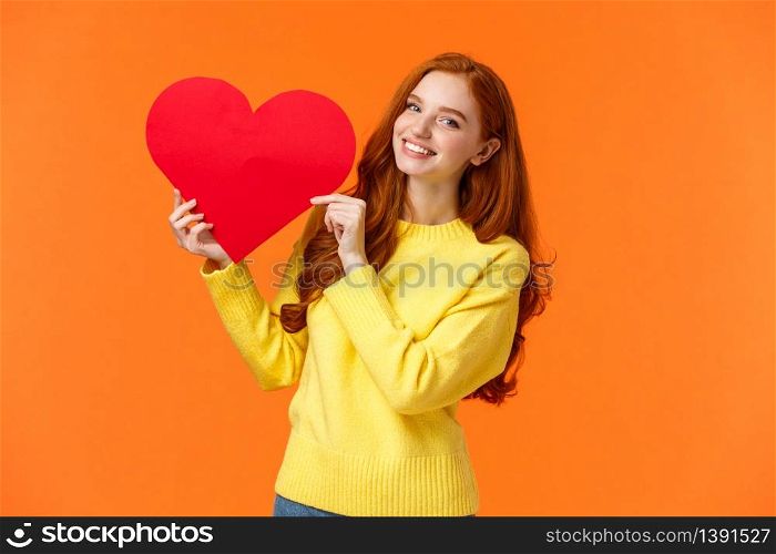 Valentines day perfect time to confess. Cute romantic and tender redhead woman in yellow sweater holding large heart sign and smiling, express affection and romance, standing orange background.. Valentines day perfect time to confess. Cute romantic and tender redhead woman in yellow sweater holding large heart sign and smiling, express affection and romance, standing orange background