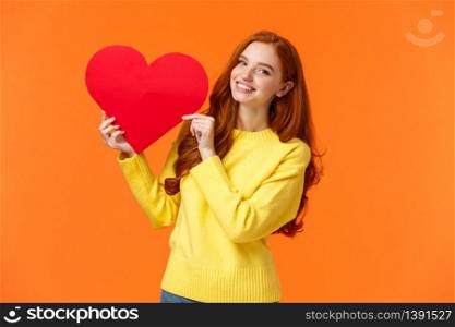 Valentines day perfect time to confess. Cute romantic and tender redhead woman in yellow sweater holding large heart sign and smiling, express affection and romance, standing orange background.. Valentines day perfect time to confess. Cute romantic and tender redhead woman in yellow sweater holding large heart sign and smiling, express affection and romance, standing orange background
