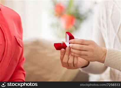 valentines day, proposal and engagement concept - man giving diamond ring in little red gift box to woman at home. man giving diamond ring to woman on valentines day
