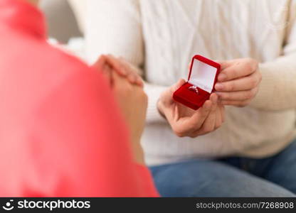 valentines day, proposal and engagement concept - man giving diamond ring in little red gift box to woman at home. man giving diamond ring to woman on valentines day