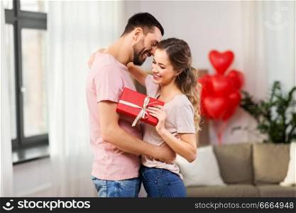 valentines day, relationships and people concept - happy couple with gift box hugging at home. happy couple with gift box hugging at home