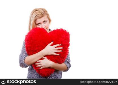 Valentines day, romance and relationship symbols concept. Uhhappy sad young woman holding big red pillow in heart shape. Sad girl holding big red pillow in heart shape