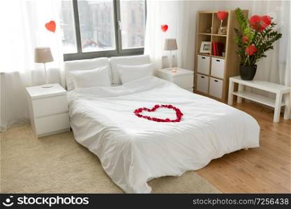 valentines day, romantic date and holidays concept - bed decorated with heart made of red petals in bedroom at home. cozy bedroom decorated for valentines day