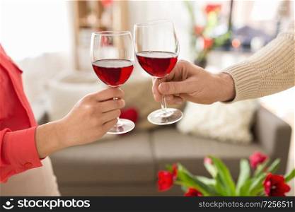 valentines day, romantic date and holidays concept - hands of couple drinking red wine and clinking glasses at home. hands of couple with red wine glasses toasting 