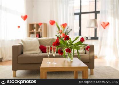 valentines day, romantic date and holidays concept - two ch&agne glasses and red tulip flowers on table in living room or home. ch&agne glasses and flowers on valentines day