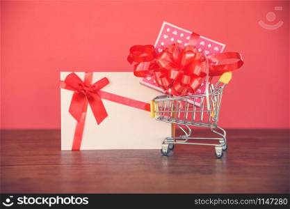 Valentines day shopping and Gift card Gift Box / Pink present box with red ribbon bow on shopping cart to Merry Christmas Holiday Happy new year or Valentines day on red background - Shopping vacation