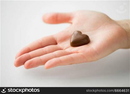 valentines day, sweets and confectionery concept - close up of hand holding heart shaped chocolate candy. close up of hand with heart shaped chocolate candy