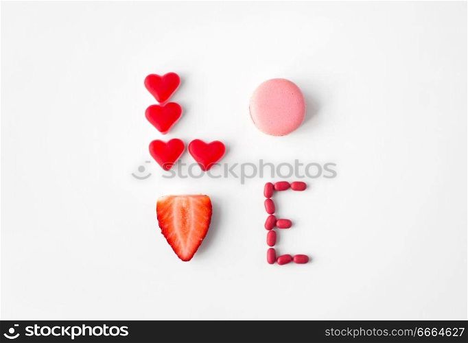 valentines day, sweets and confectionery concept - close up of word love made of red heart shaped candies, pink macaron cookie and strawberry. close up of word love made of sweets