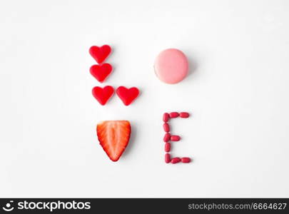 valentines day, sweets and confectionery concept - close up of word love made of red heart shaped candies, pink macaron cookie and strawberry. close up of word love made of sweets