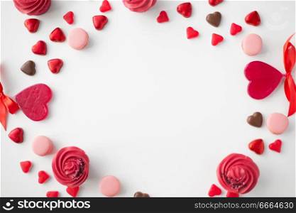 valentines day, sweets and romantic concept - close up of frosted cupcakes, red heart shaped chocolate candies, macarons and lollypops on white background. close up of sweets on valentines day