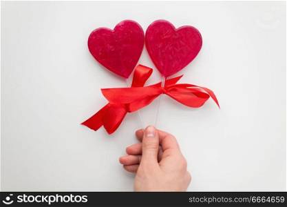 valentines day, sweets and romantic concept - close up of hand holding red heart shaped lollipops on white background. close up of hand holding red heart shaped lollipop