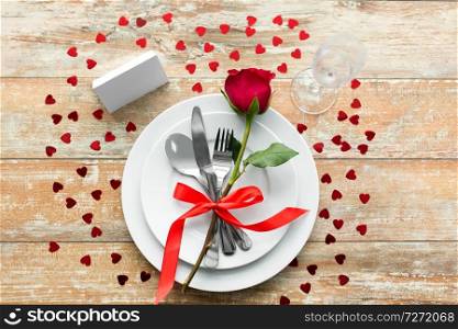 valentines day, table setting and romantic dinner concept - close up of red rose flower on set of dishes with cutlery, red rose, hearts and blank place card on wooden background. close up of table setting for valentines day