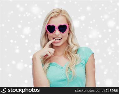 valentines day, winter holidays, christmas and people concept - smiling young woman or teenage girl in heart shaped sunglasses over snow