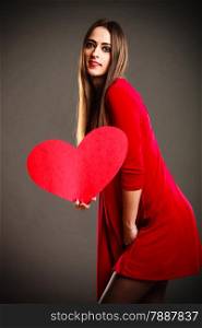 Valentines Day. Woman in red dress holding heart sign love symbol on grey background in studio.